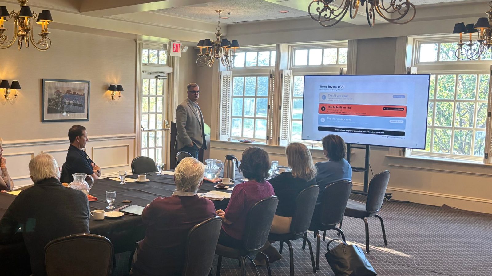 Brian presenting a slide on the three layers of AI to a group of career coaches seated around a conference table